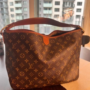 Louis Vuitton Monogram axelväska - Säljer en klassisk Louis Vuitton axelväska i brunt skinn med ikoniskt monogrammönster. Väskan har bred axelrem i läder, guldfärgade metalldetaljer och rymligt huvudfack. Perfekt för dig som vill ha en tidlös och lyxig accessoar med tydlig logga. Modellen heter Delightful pm elleroch går runt 16 000kr begagnad men pågrund av att jag bara har kvitto kvar så säljer jag min för 10 600