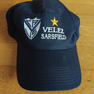 Velez Sarsfield marinblå keps Argentinsk fotbolls klubb - Marinblå keps med broderad Velez Sarsfield-logga och gul stjärna framtill. Kepsen har böjd skärm och justerbar baksida. Tillverkad i bomull, perfekt för dig som gillar fotboll och vill visa ditt lag. Snygg och sportig stil med vit och blå brodyr.