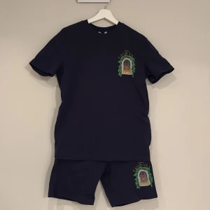 Mörkblå t-shirt från Casablanca - Mörkblå t-shirt och shorts från Casablanca med färgglad tryckt grafik på bröstet och ryggen. Klassisk passform med rund hals och korta ärmar. Tillverkad i mjuk bomull, perfekt för en avslappnad och trendig look.