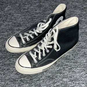 Svarta Converse Chuck Taylor All Star - Klassiska svarta Converse Chuck Taylor All Star med vita snören och tåhätta. Skorna har hög modell, vit sula och tydliga kontrastsömmar. Perfekta för en avslappnad och tidlös streetstil.