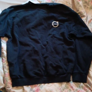 Svart Volvo-tröja från Berendsen L - Svart långärmad tröja från Berendsen i storlek L med klassiskt Volvo-märke broderat på bröstet. Tröjan har rund hals och är tillverkad i mjukt material som känns skönt mot huden. Perfekt för dig som gillar stilren och enkel design.