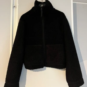 Svart teddyjacka från H&M - Mysig svart teddyjacka från H&M med hög krage och dragkedja framtill. Jackan har två stora fickor och är tillverkad i fluffigt teddy-material. Perfekt för kyliga dagar 💕