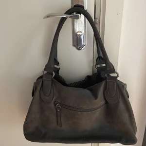 Svart axelväska i skinn med stjärndetaljer - Snygg svart axelväska i skinn med perforerade partier och små stjärnor som detalj. Väskan har flera fack, dragkedja framtill och coola metalldetaljer på sidorna. Invändigt finns mönstrat tyg och extra fickor för småsaker. Perfekt för dig som gillar stilrena accessoarer med edge.❤️