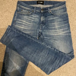 Blå jeans från BLK DNM - Snygga blå jeans från BLK DNM med klassisk femficksdesign och subtila slitningar framtill. Jeansen har en rak passform och normal midja, tillverkade i mjukt bomullsmaterial för skön känsla. Perfekt för dig som gillar en stilren och avslappnad look. Nypris 1900