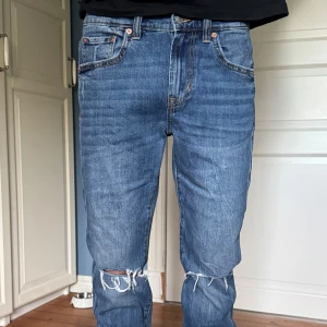 Jeans med hål i knäna - Säljer ett par blå slim fit jeans från 157 med klassisk femficksdesign och snygga slitningar vid knäna. Jeansen har normal midja, raka ben och är tillverkade i bomullsdenim. Tveka inte att höra av dig vid frågor!