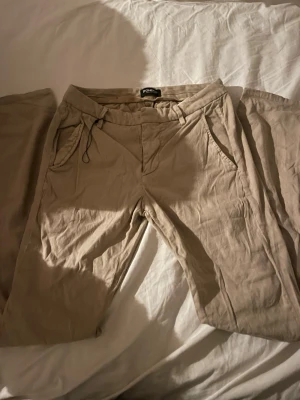  Chinos Byxor från Dondup - Snygga chinos byxor från Dondup, tillverkade i Italien. Byxorna har klassisk rak passform, sidfickor och bakfickor med knapp. Materialet är bomull och de har bälteshällor samt en liten metall-detalj vid fickan. Perfekta för en clean och chill stil.