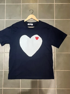 Comme des Garçons Play t-shirt - Navy färgad t-shirt från Comme des Garçons Play med stort vitt hjärta och rött hjärtdetalj med ögon på bröstet. Klassisk rund hals och korta ärmar. Tillverkad i mjuk bomull som känns skön mot huden. 