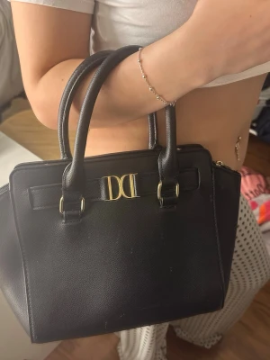 Svart handväska med gulddetaljer - Jätte fin handväska med gulddetaljer från don Donna. Axelrem saknas! Bra skick men är sliten på handtagen