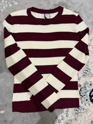 Randig vinröd och vit tröja JDY - Säljer en ribbad långärmad tröja från JDY i storlek S. Tröjan har breda horisontella ränder i vinrött och vitt, rund hals och figurnära passform. Materialet är mjukt och stretchigt, perfekt för dig som gillar en enkel men snygg look. Den är helt nytt och ordinarie priset är 400. 