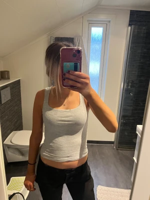 Grå linnetopp med breda axelband - Säljer en enkel och stilren grå linnetopp med breda axelband och rundad halsringning. Toppen är figurnära och har en mjuk, stretchig känsla som gör den skön att bära. Perfekt för dig som gillar en clean look och vill ha något som är lätt att matcha.