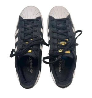 Adidas Superstar svart/vit strl 36 - Klassiska Adidas Superstar sneakers i svart med vita ränder och gummitå. Skorna har snörning, gulddetaljer på plösen och en platt sula. Perfekta för dig som gillar streetstyle och tidlös design. Är inte mer än testade. Stått i förrådet…