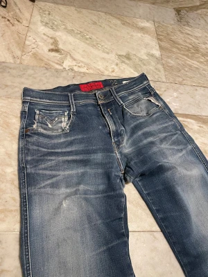 Replay Anbass jeans blå slim fit - Snygga Replay Anbass jeans i blå tvätt med slitningar och klassiska fickor. Slim fit modell. Jeansen har detaljerade sömmar och Replay-logga på bakfickan. St 28/32, Perfekta för dig som gillar en modern och avslappnad stil. Mvh Henry 