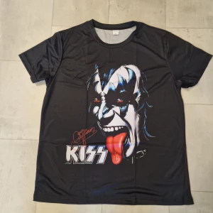 Svart KISS t-shirt med tryck - Cool svart t-shirt med stort tryck av Gene Simmons från KISS på både fram- och baksidan. T-shirten har korta ärmar och är gjord i mjuk polyester som känns skön mot huden. Perfekt för dig som vill sticka ut med en ikonisk rockstil.