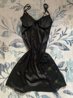 Satinklänning - Svart satinklänning/nattlinne med mesh och broderi-detaljer längs sidorna och bysten och snörning i ryggen. Strl: L, justerbar tack vare snörningen. Så otroligt vacker men knappt använd, i väldigt bra skick. Läs gärna bion innan köp. 