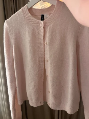 Ljusrosa kofta från H&M - Superfin ljusrosa kofta från Divided med rund hals och knappar framtill. Mjuk stickad känsla och ribbade muddar vid hals, ärmslut och nederkant. Perfekt att slänga över en topp när det är lite kyligt ute.