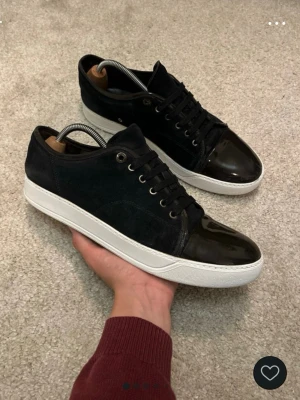 Lanvins - Snygga svarta sneakers med vit sula och lackad tådel. Ovandelen är i mocka och skorna har klassisk snörning. Perfekta för dig som vill ha en stilren men ändå unik look. Passar till det mesta och ger en clean vibe.