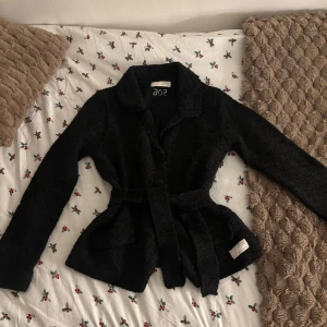 Svart stickad cardigan Odd Molly - Mysig svart stickad cardigan jacka från Odd Molly med bälte i midjan och stora knappar framtill. Jackan har krage och två fickor. Tidlös och enkel att matcha med allt.