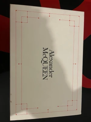 Svarta Alexander McQueen sneakers - Säljer ett par svarta Alexander McQueen sneakers med vit detalj på hälen. Skorna har rund tå, platt sula och klassisk snörning. Medföljer extra svarta skosnören med vit mönster. Snygg och stilren design som lyfter din outfit.