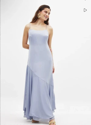 Ljusblå långklänning - Den här klänningen har en flowy fit, tunna axelband med en justerbar knappstängning och en gömd sidodragkedja. Klänningen har ett foder på den övre hälften. Modellen har storlek 36. Aldrig använd, prislapp kvar. Köpt för 599 kr. Säljs inte längre. I satin. 