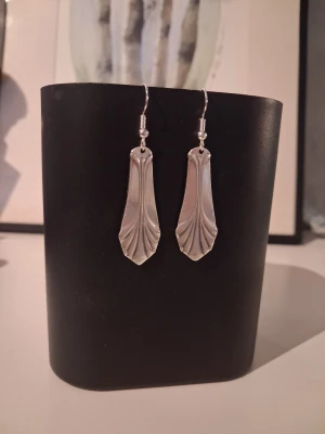 Handgjorda örhängen återbruk  - Egentillverkade örhängen skapade av 2st skedar gjorda i nysilver. Örhänget är 3.5cm långt, öronkroken är nickelsäker och aldrig använd. Blir en unik och elegant accessoar till outfiten.