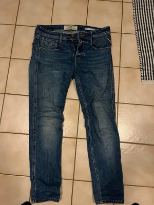 Replay Anbass jeans blå W29 L30 - Säljer ett par snygga Replay Anbass jeans i klassisk blå tvätt. Det står att jeans är 29/32 men det stämmer ej då de blivit nerkortade hos en skräddare så de passar dem som är 165-170. Priset kan diskuteras vid smidig affär😃