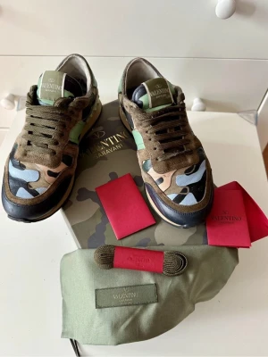 Valentino Garavani Rockrunner sneakers - Säljer ett par Valentino Garavani Rockrunner sneakers med camouflagemönster i grönt, beige, svart och ljusblått. Skorna har snörning, platt sula och detaljer i mocka och skinn. Ikoniska nitar på hälen och logga på plösen. Medföljer extra skosnören och dustbag.