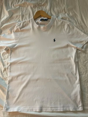 Ralph lauren T-shirt - Vit t-shirt från Polo Ralph Lauren med klassisk rund hals och korta ärmar. T-shirten har en liten broderad logga i marinblått på bröstet och är gjord i mjuk bomull. Perfekt basic-plagg med clean look och snygg passform. Passar S och M. Pris går att diskutera 