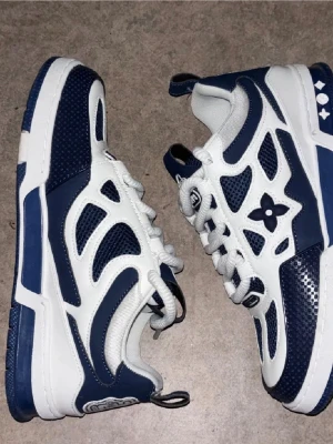 LW skor - Säljer ett par Loui V sneakers i marinblått och vitt med snygga meshpaneler och skinnpartier. Skorna har rund tå, platt sula och klassisk snörning. Ikoniska detaljer plösen och sidan. Perfekta för dig som vill sticka ut med lyxig streetstyle.