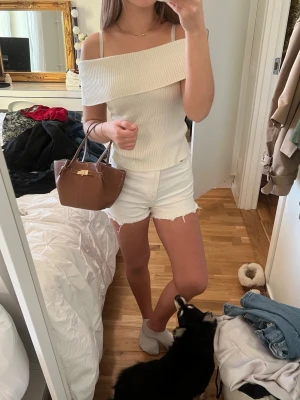 Vit ribbad offshoulder topp - Säljer en vit ribbad topp med offshoulder-design och smala axelband. Toppen har en bred, vikt kant över axlarna och är figurnära med en croppad passform. Perfekt för sommarens alla tillfällen och enkel att matcha med shorts eller jeans.