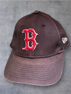 Svart Boston Red Sox keps från New Era - Säljer en svart keps från New Era, modell 9FORTY, med broderad röd Boston Red Sox-logga framtill och vit New Era-logga på sidan. Kepsen har böjd skärm och justerbar rem baktill. Materialet är bomull och insidan har märkning med Genuine Merchandise.