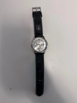 Casio klocka  - Casio armbandsur för unisex med svart läderarmband och rund urtavla i silverfärg. Klockan har en analog display och klassisk design.