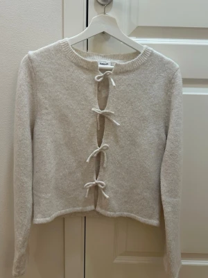 Beige kofta med knyt från Kappahl - Mysig beige kofta från Kappahl med fyra knyt framtill. Koftan är endast använd 3 gånger och tvättad 1 gång så den är i väldigt bra skick! Säljer för den inte kommer till användning!