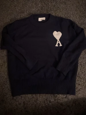 Mörkblå stickad tröja från Ami Paris - Säljer en mörkblå stickad tröja från Ami Paris. Storleken är S. Den är i bra skick men de finns två trådar som sticker ut på vänster axel som ni kan se på bild två men de märks knappt. Hör av er vid frågor!