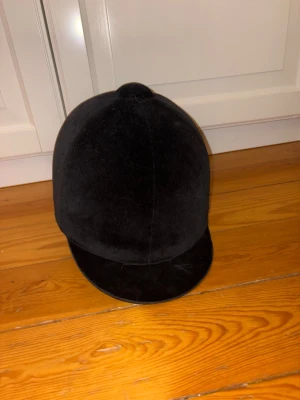 Svart ridhjälm med sammet - Säljer en klassisk svart ridhjälm med sammetsyta och dekorativ rosett baktill. Hjälmen har rundad form, justerbara remmar och röd mjuk insida för en nättre passform! Köp nu jag postar snabbt!!💕💗