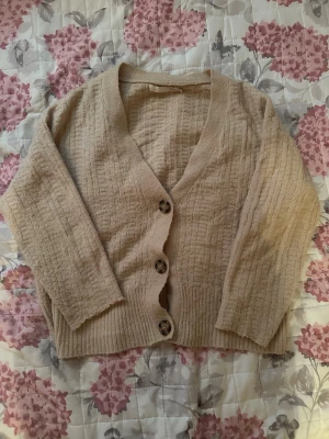 Beige kofta från lager  157 XS - Mysig beige kofta från lager 157 i storlek XS. Koftan har ett ribbat mönster, v-ringad hals och tre stora knappar framtill. Materialet känns mjukt och är perfekt för lager-på-lager. Passar dig som gillar en enkel och chill stil.