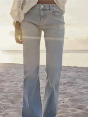 Bootcut lågmidjade ljusblå zara - Säljer ett par ljusblå bootcut jeans med klassisk femficksdesign och knappgylf. Jeansen har en låg midja och är tillverkade i mjukt denimtyg som ger en skön passform. Perfekta för dig som gillar retrovibbar och vill ha en avslappnad look.