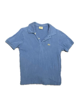Lacoste piké - Säljer en klassisk blå pikétröja från Lacoste med korta ärmar och krage. Tröjan har två knappar framtill och den ikoniska krokodilloggan broderad på bröstet. Materialet är mjuk bomull som känns skönt mot huden. Perfekt för dig som gillar stilren och sportig look. Storlek 14 yrs men passar XS😊 Skriv vid funderingar 📲🤩