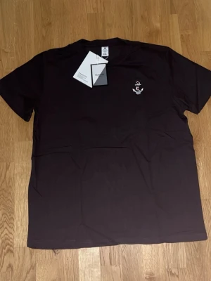 Svart t-shirt med ankare från Fashion - Svart t-shirt från Fashion i storlek 3XL, tillverkad i mjuk bomull. På bröstet finns ett litet broderat ankare i vitt och rött som ger en cool marin vibe. Klassisk rund hals och korta ärmar, perfekt för chill dagar.