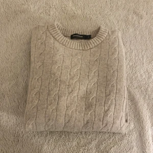 Beige stickad tröja från Dressmann - Säljer en beige stickad tröja från Dressmann i storlek M men tyvärr så har tröjan krympt i tvätten så den passar dem som är runt 165-175 typ Tröjan har ett klassiskt flätmönster, rund halsringning och ribbade muddar vid ärmslut och nederkant. Perfekt för dig som gillar en enkel och stilren look.