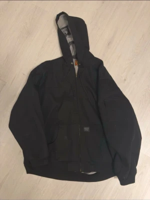 Svart höst/vinter jacka från Fb County  - Svart jacka från County FB med grått innerfoder och tryckt logga på insidan. Jackan har huva med snörning, dragkedja framtill och stora fickor. Perfekt för dig som gillar streetwear och vill ha en chill look.