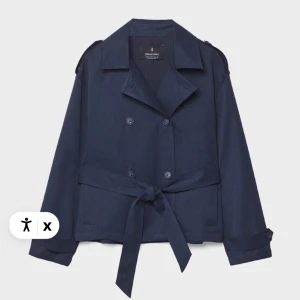 Mörkblå trenchcoat från Stradivarius - Snygg mörkblå trenchcoat från Stradivarius med klassisk krage, dubbelknäppning och bälte i midjan. Jackan har långa ärmar och stilrena knappar framtill. Perfekt för dig som vill ha en cool och tidlös look.