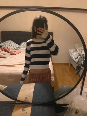 Randig stickad tröja  - Säljer en croppad stickad tröja från Lager 157 i storlek S. Tröjan har breda marinblå och vita ränder, rund halsringning och långa ärmar. Perfekt för dig som gillar en chill och trendig stil.