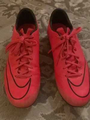 Röda Nike fotbollsskor med dobbar - Säljer ett par röda Nike fotbollsskor med svarta detaljer och klassisk Nike-logga på sidan. Skorna har snörning och dobbar för bra grepp på planen. Perfekta för dig som vill sticka ut på matchen!