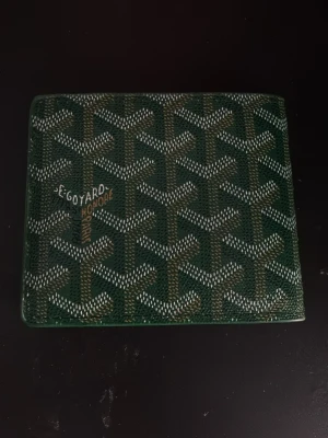 Grön plånbok i skinn med mönster - Snygg grön plånbok i skinn med diskret mönster på utsidan. Plånboken har flera kortfack och ett fönster för ID-kort. Perfekt storlek för att få plats med allt du behöver i vardagen.