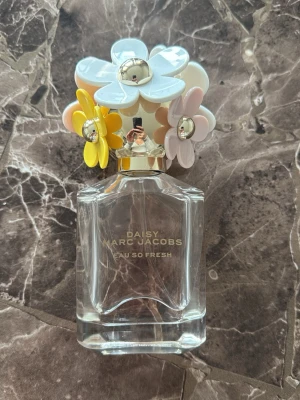 Daisy Marc Jacobs Eau so Fresh parfym (~65ml) - Daisy Eau So Fresh från Marc Jacobs är en ungdomlig parfym i en genomskinlig glasflaska med ett unikt blommigt lock. Doften är söt, med många olika inslag som passar perfekt årets alla månader. Endast använd ett fåtal gånger, original är 75ml och uppskattar där är kvar ~65ml.  Toppnoter:  Hallon, grapefrukt, päron  Hjärta:  Viol, vild ros, äpple  Basnoter:  Mysk, cederträ, plommon