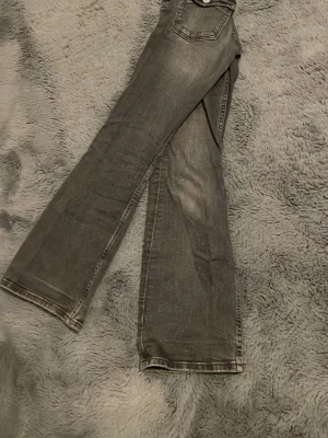 Grå bootcut jeans - Säljer ett par grå bootcut jeans med snygga fickor. Jeansen har en lätt utsvängd passform nedtill och är perfekta för dig som gillar en avslappnad men ändå trendig look.