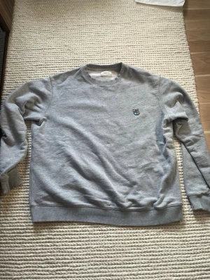 Grå sweatshirt från Tonsure XL - Säljer en grå sweatshirt och en T-shirt långärmad från Tonsure i storlek XL. Tröjan har ett färgglatt broderat björnhuvud på bröstet och klassisk rund halsringning. Tillverkad i mjuk bomull och har ribbade muddar vid ärmar och nederkant. Perfekt för en clean och chill look.