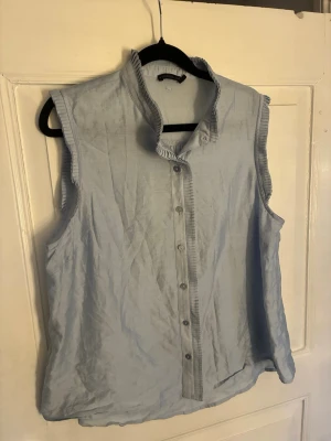 Ljusblå ärmlös blus från Stockh LM - Snygg ljusblå blus från Stockh LM med ståkrage och knappar framtill. Blusen är ärmlös och har fina detaljer längs kragen och knappslån. Tillverkad i ett lätt och luftigt tyg, perfekt för varma dagar. Nypris 599kr.