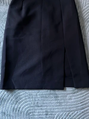 Svart pennkjol med slits - Stilren svart pennkjol med slits framtill. Kjolen har en klassisk, rak passform och bälteshällor i midjan. Perfekt till en snygg topp eller skjorta. 