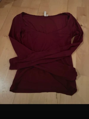 Mörkröd långärmad topp H&M - Säljer en mörkröd långärmad topp från Nelly med v-ringad halsringning. Toppen är i mjuk bomull och har en enkel, slim passform som sitter snyggt på kroppen. Perfekt att styla med jeans eller kjol för en clean look.